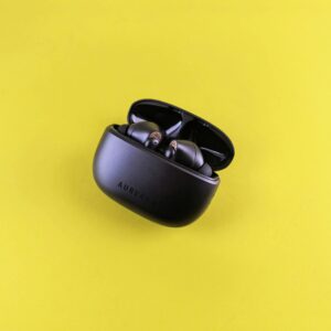 Close-up of modern black wireless earbuds in charging case on a vibrant yellow background.