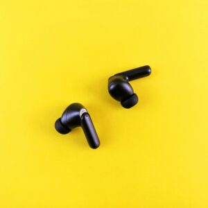 Minimalist black wireless earbuds on a bright yellow backdrop for tech and lifestyle themes.