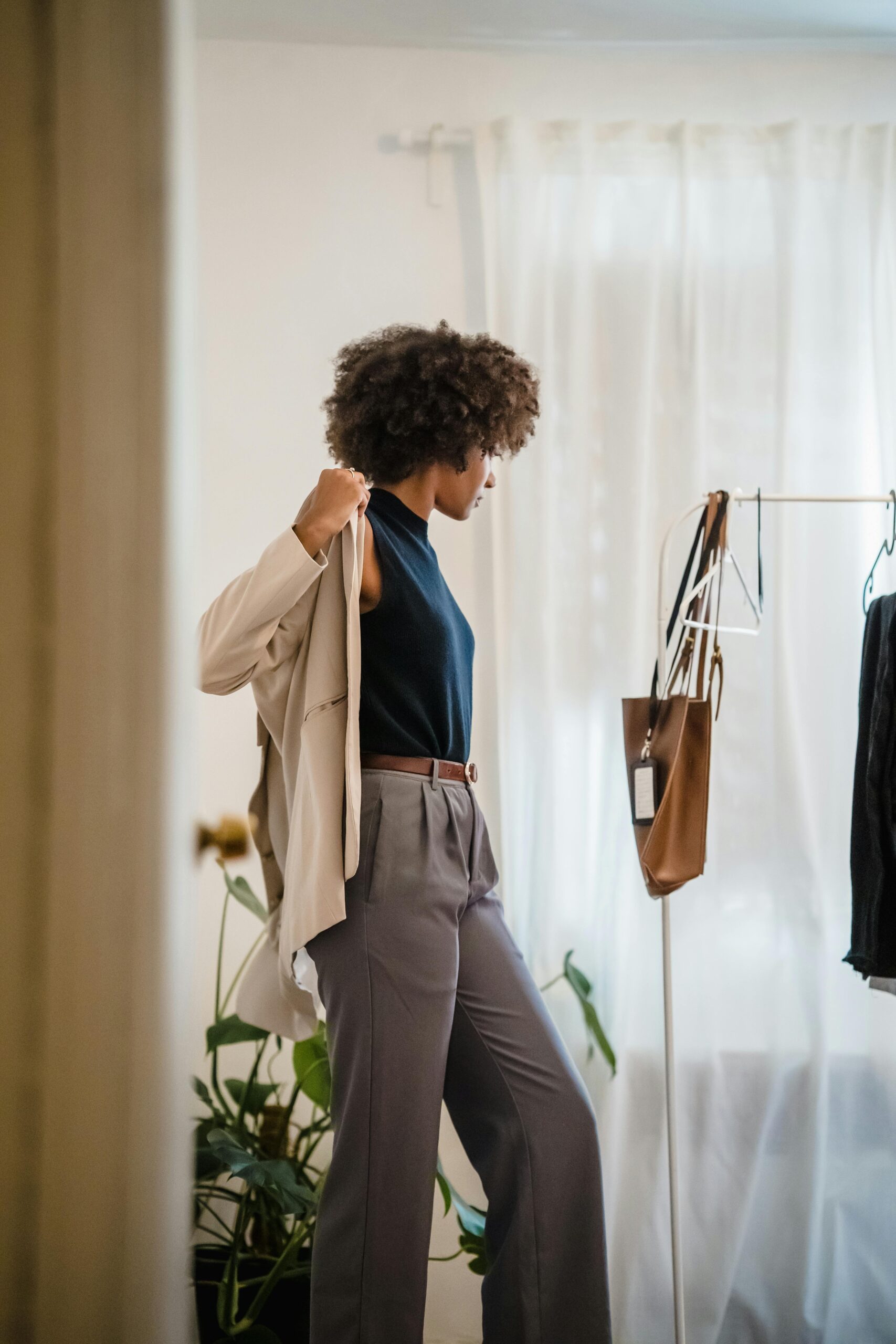 Fashionable woman dressing in stylish room. Modern interior, plants, and wardrobe details.
