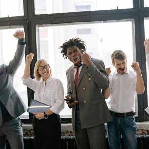 Group of diverse professionals celebrating achievement in office setting with enthusiasm.